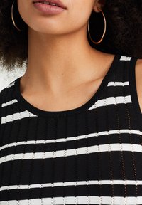 Randig stickad linne i svart och vitt med ribbat mönster, bred rundad halsringning och öppen vävning genom hela tyget.