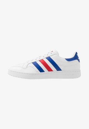 Baskets basses blanches Adidas avec des bandes bleues et rouges sur le côté, semelle blanche et languette de talon bleue avec logo.
