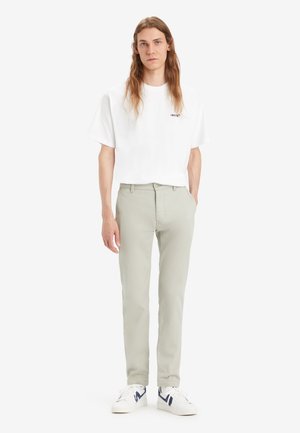 Chinos verde claro con corte recto, combinados con una camiseta blanca de cuello redondo que presenta un pequeño logo negro, y zapatillas blancas.