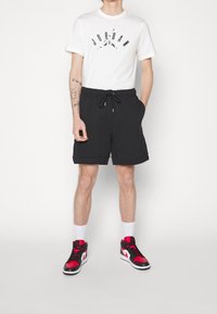 Svarta shorts med dragsko, kombinerat med en vit t-shirt som har en svart "JORDAN"-logotyp och röda samt svarta sportiga sneakers.