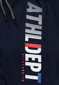 Shorts de sport navy avec "ATHLDEPT" en lettres blanches et texturées. Accents rouges et bleus. Comprend un cordon de serrage réglable et une poche latérale.