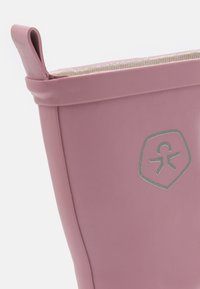 Botte en caoutchouc rose avec un extérieur texturé, un emblème argenté et une languette en haut pour une mise enfilage facile. Doublure intérieure lisse.