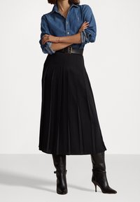 Gonna midi plissettata nera con una texture liscia, abbinata a una camicia di denim e stivali neri con tacco al ginocchio. Presenta una cintura in vita.