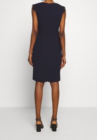 Robe marine à manches courtes avec des accents en dentelle. Taille cintrée et longueur genou, fabriquée en tissu lisse. Fermeture éclair au dos, lignes épurées.