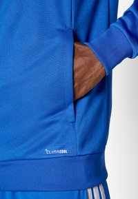 Μπλε αθλητικό φούτερ με υφασμάτινη υφή, που διαθέτει τσέπη καγκουρό και ριμπ μανσέτες. Λογότυπο "CLIMACOOL" κοντά στο τ ελείωμα.