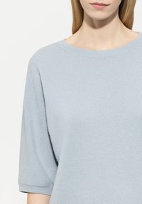 Helles blaue, gestrickte Pullover mit rundem Ausschnitt und kurzen Ärmeln, der eine weiche Textur und Rippdetails am Kragen und an den Manschetten aufweist.