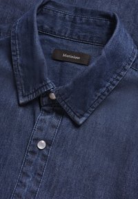 Camisa de mezclilla azul oscura con un cuello estructurado, botones de plástico y una etiqueta con el texto "Matinique" cosida en el interior del cuello.