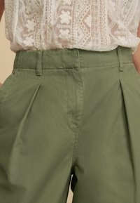 Groene geplooide broek van lichtgewicht stof, met zijzakken en een soepele textuur, gecombineerd met een delicate witte geborduurde top.