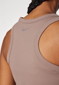 Aansluitende sportieve tanktop van lichtbruin stof, met een ronde halslijn, brede schouderbanden en een klein grijs Nike-logo op de achterkant.