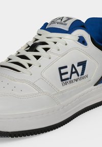 Λευκό και μπλε sneaker EA7 Emporio Armani με λευκά κορδόνια και λογότυπο της μάρκας στο πλάι και στη γλώσσα, με μαύρο περίγραμμα στη σόλα.