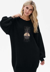 Czarna, oversize bluza z długimi, bufkami rękawami. Posiada centralny nadruk drzewa z korzeniami na tle żółtego słońca.