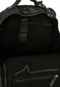 Interno di uno zaino in pelle nera con una tasca con zip, foderato in tessuto e una toppa con logo a forma di ancora. Molti scomparti per l'organizzazione.