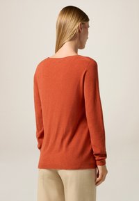 Pull couleur rouille en matériau doux, avec des manches longues, une coupe décontractée et un col rond. Tissu texturé avec des poignets côtelés.