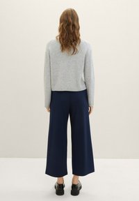 Grå, ribbad tröja med en kort design i kombination med vida, marinblå byxor. Svarta skor fulländar outfiten.