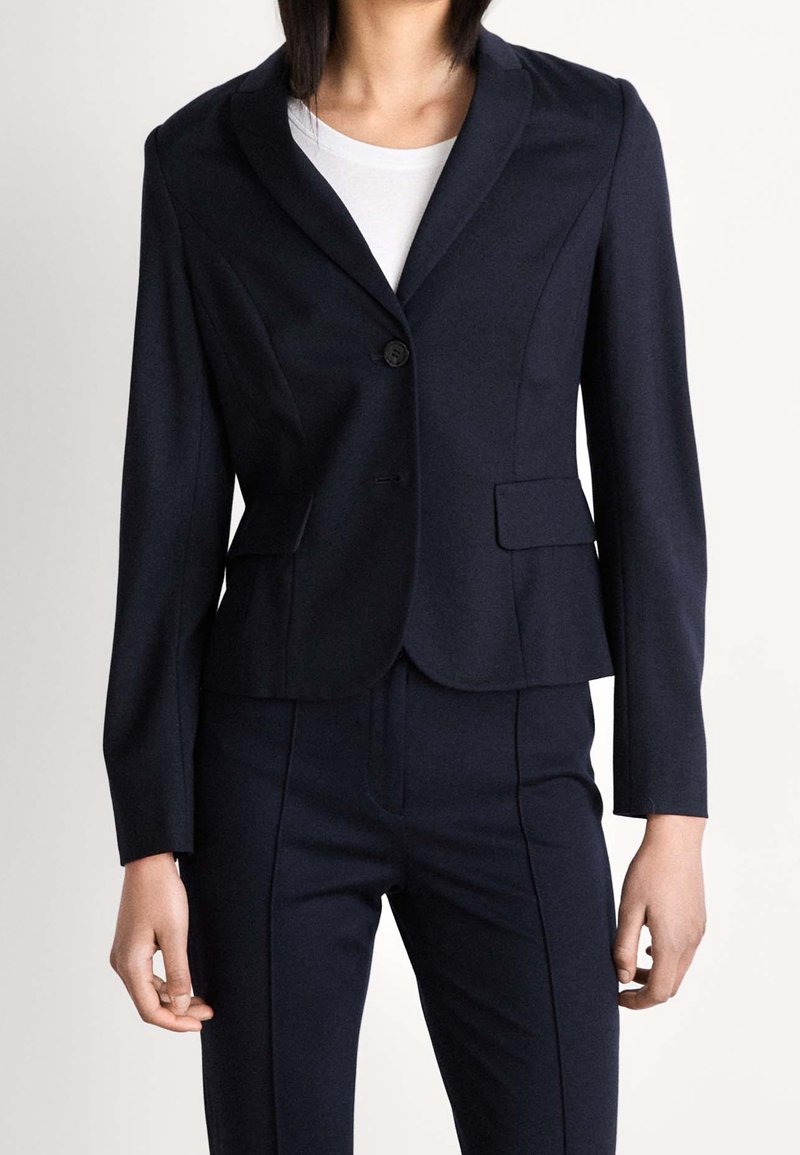 Blazer bleu marine en tissu lisse, doté d'un col à revers cranté, d'une fermeture à un bouton et de deux poches avant, avec une silhouette ajustée.