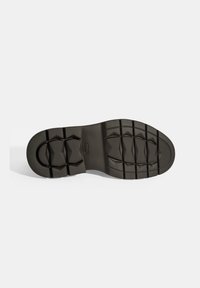 Zwarte rubberen zool met een gestructureerd patroon van hoekige vormen en diepe groeven voor grip. Ronde hak.