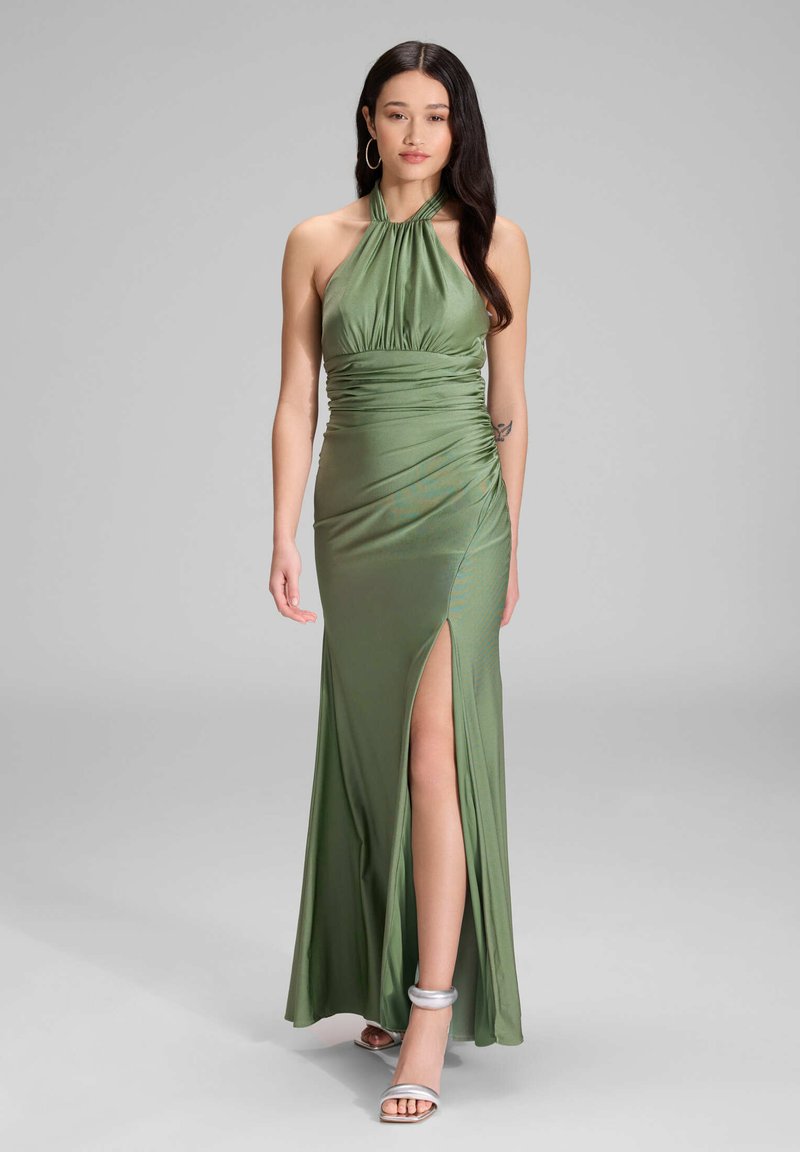 Robe halter verte avec un design froncé, fente sur le côté et tissu lisse et fluide. Associée à des sandales à bride de cheville argentées.