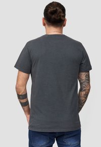 Grå bomulds t-shirt, kortærmet, rund hals. Har synlige sømme og en afslappet pasform. Bæres med blå denimbukser.