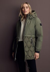 Doudoune verte olive avec une partie supérieure lisse, une partie inférieure matelassée, des poches zippées et une capuche à cordon de serrage ajustable.