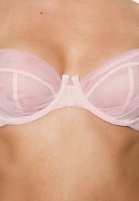 Sutiã com aro em rosa claro, com copas em rede, costuras verticais e um pequeno detalhe de corte no centro. Faixa de tecido suave e alças ajustáveis.