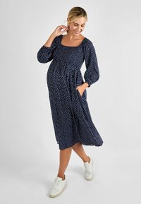 Navy-blå midi-kjole med hvite prikker, firkantet utringning, ballongsleeves og sidelommer. Brukt med hvite sneakers.