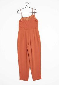 Rust-colored jumpsuit with spaghetti straps, zipper closure, tailored waist, and straight-leg design. Smooth texture, minimal accents.