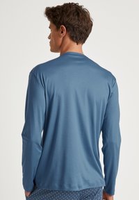 Langarm blauwe shirt gemaakt van zachte stof, met een ronde hals en een relaxte fit. De achterkant toont een gladde textuur en subtiele stiksels.