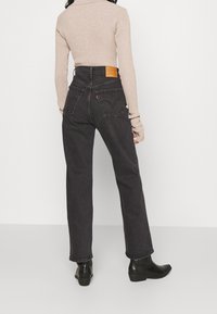 Jeans negros de alta cintura con un corte recto, que presentan un parche de cuero en la parte posterior, costuras en contraste y dos bolsillos traseros.