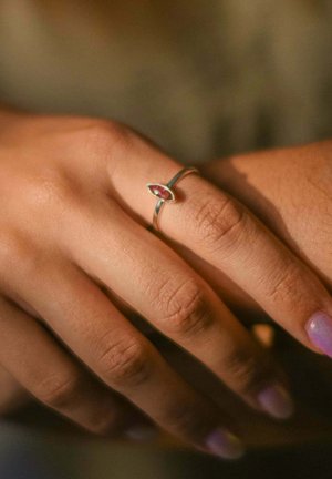 Anello d'argento con un centro in granato ovale, caratterizzato da una fascia liscia e delicate incisioni, posato su una mano con pelle di colore marrone chiaro.