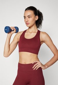 Top deportivo corto burdeos con textura acanalada, leggings de tiro alto a juego y una mancuerna azul en la mano, destacando la ropa deportiva.