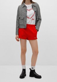 Sort og hvid houndstooth jakke, hvid T-shirt med rød print, røde shorts, sorte ankelstøvler, hvide sokker med røde detaljer.