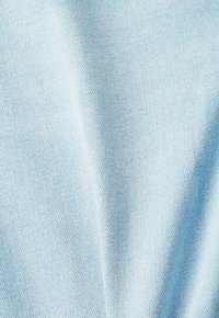 Tissu en denim bleu clair avec une texture tissée diagonale visible et des plis doux créant des ombres légères.
