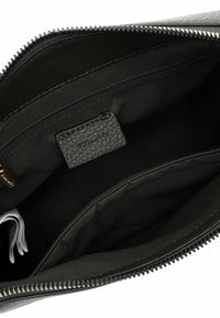 L'interno della borsa in pelle nera presenta una fodera in tessuto morbido, una tasca con zip e un piccolo etichetta testurizzata. Design semplice e funzionale.