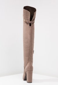 Bota de ante sintético color topo hasta la rodilla con puntera redondeada, tacón cuadrado, correa decorativa con hebilla y cremallera en la parte trasera para facilitar el uso.