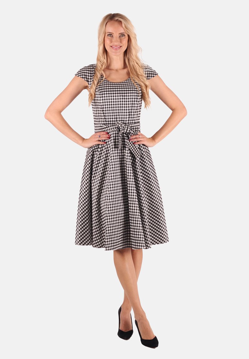 Schwarzes und weißes Gingham-Kleid mit kurzen Ärmeln, tailliertem Oberteil und ausgestellt Rock; hat eine gebundene Taille und saubere Nähte.