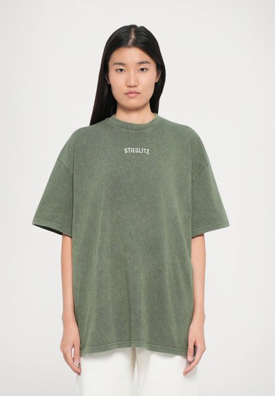 Oversized groene t-shirt gemaakt van zacht, gestructureerd materiaal. Voorzien van een ronde hals en witte "STIEGLITZ" tekst gedrukt op de voorkant.