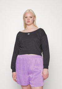 Sweatshirt preto cropped com mangas longas, decote amplo e logótipo branco; combinado com calções soltos de cetim lilás claro. Textura suave.