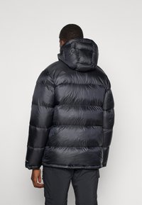 Schwarze Daunenjacke mit abnehmbarem Kapuze, ausgestattet mit gesteppten Abschnitten, glänzender Textur und elastischen Bündchen, entworfen für Wärme und Komfort.