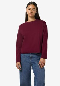 Top bordeaux a maniche lunghe con scollatura rotonda e vestibilità comoda, abbinato a jeans a gamba larga di colore azzurro chiaro. Tessuto dall'aspetto morbido.