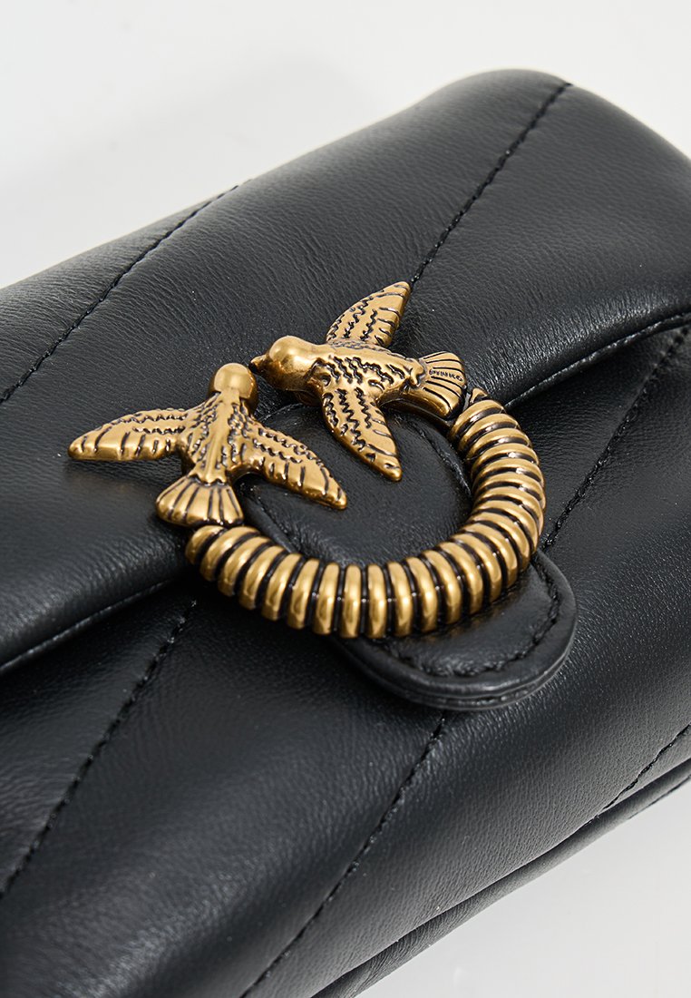 Portefeuille en cuir noir avec un accent en métal doré représentant un oiseau et un ressort sur le rabat, et des détails de couture verticale sur le corps.