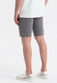 Shorts élastiques gris avec une texture lisse, de longueur mi-cuisse et un petit logo au niveau de l'ourlet. Associés avec des chaussures de sport blanches.