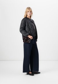 Žena oblečená v černé prošívané bundě, širokých tmavých džínách, černých balerínách a nese malou tmavě hnědou crossbody kabelku.