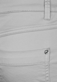 Jeans de un gris claro con una textura suave, que presentan costuras sutiles, un pequeño bolsillo para monedas y un detalle de remache metálico.