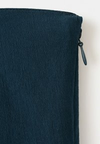 Pochette en tissu texturé bleu foncé avec fermeture éclair fermée et bord supérieur légèrement incurvé sur fond blanc.