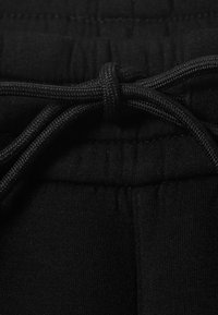 Primer plano de pantalones de chándal negros con cintura elástica y nudo en el cordón atado.
