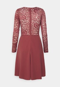 Vestido Marlowe com mangas longas de renda em bordô, apresentando uma saia sólida e fecho éclair nas costas. A renda possui detalhes de padrão floral.