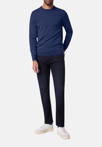 Marineblauer Strickpullover mit Rundhalsausschnitt, langen Ärmeln und gerippten Bündchen, kombiniert mit dunklen Jeans und weißen Sneakers. Einfaches Design, ohne Muster.