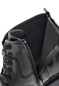 Botín negro de cuero hasta el tobillo con una superficie texturizada, que cuenta con una cremallera lateral, ojales para cordones y un forro interior suave visible.