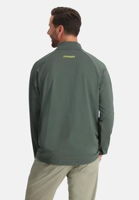 Chemise verte à manches longues avec un motif texturé, dotée d'un col montant et du logo "SPYDER" en jaune à l'arrière.