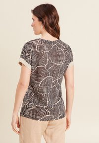 Zwart en beige kortmouwen top met een abstract bladerenpatroon, lichtgewicht stof en een ronde halslijn met contrasterende afwerking.